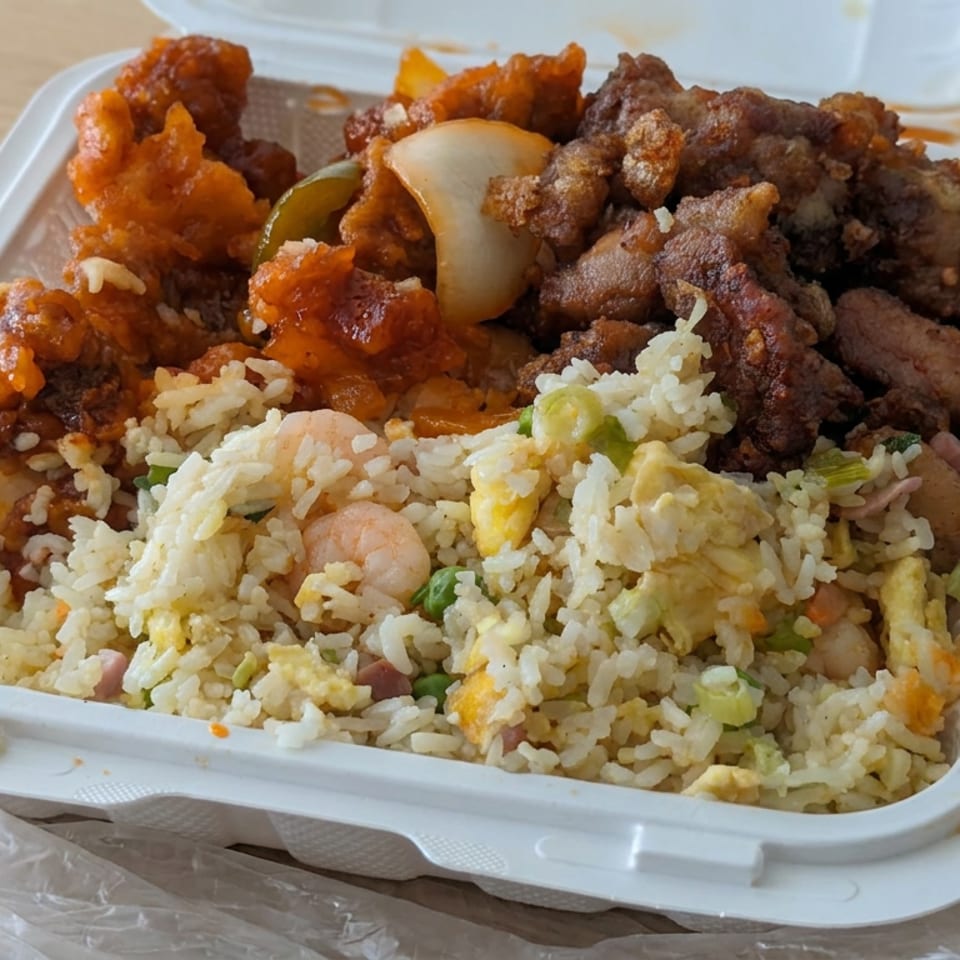 Takeout container filled with fried rice, shrimp, vegetables, sweet-and-sour chicken, and crispy fried meat on a wooden table.